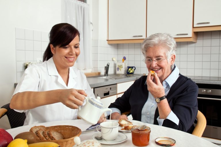 a geriatric nurse helps elderly woman at breakfast